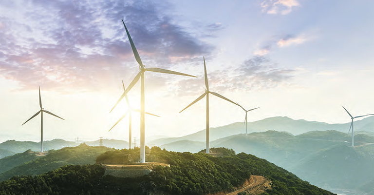 Wind turbines on green hills at sunrise against mountain range