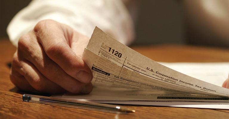 Person holding a U.S. IRS Form 1120 on a desk with a pen
