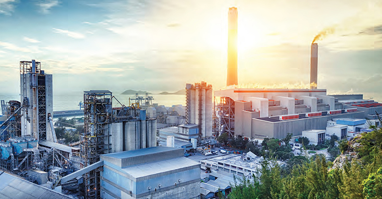 Large industrial plant with smoke stacks emitting steam, overlooking water