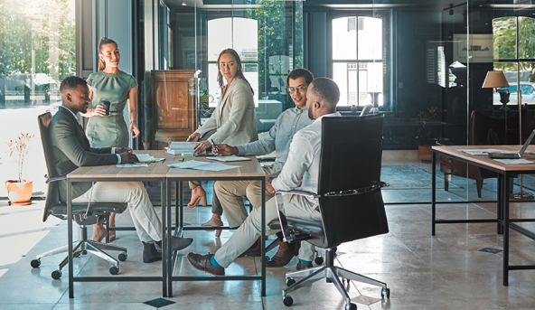 Three men sitting around table, two women standing at table