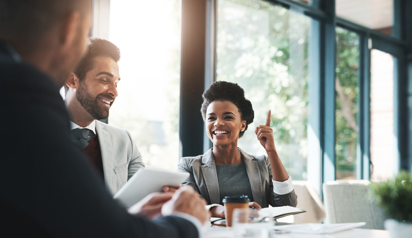 Three business professionals in a meeting, with one woman raising her finger to share an idea