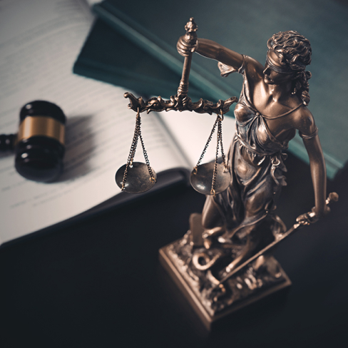 Lady Justice statue with scales and sword on a desk beside legal documents, folders, and a judge’s gavel