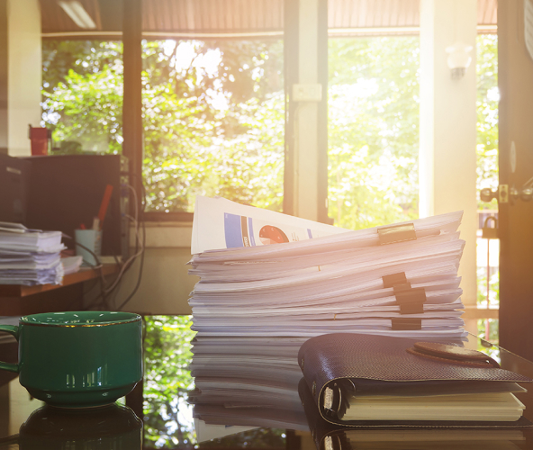 Stack of documents on a desk with a notebook and green coffee mug