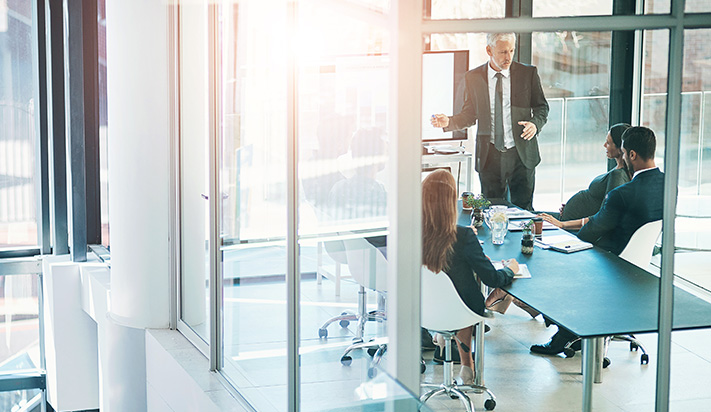Business meeting in a modern office with a man presenting to three seated colleagues, to symbolize prerogatives of control