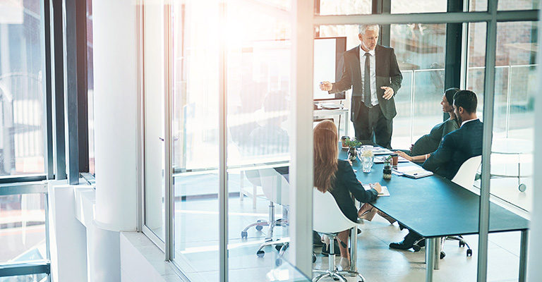 Business meeting in a modern office with a man presenting to three seated colleagues, to symbolize prerogatives of control